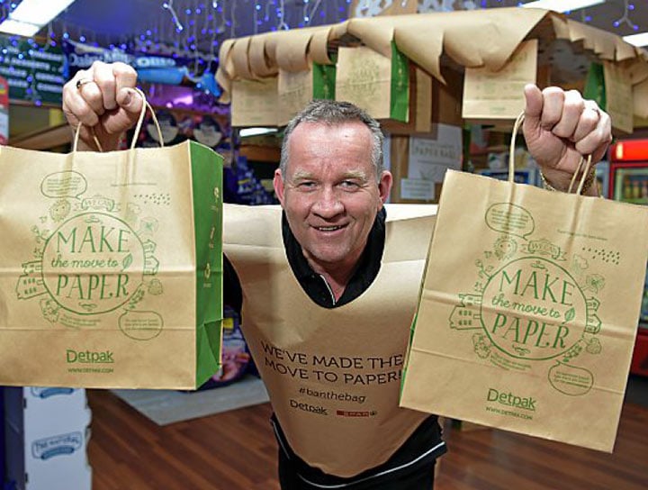 Image of Bruce Lutcherhead smiling and holding paper bags. He is also wearing an outfit made out of a large paper bag. 
