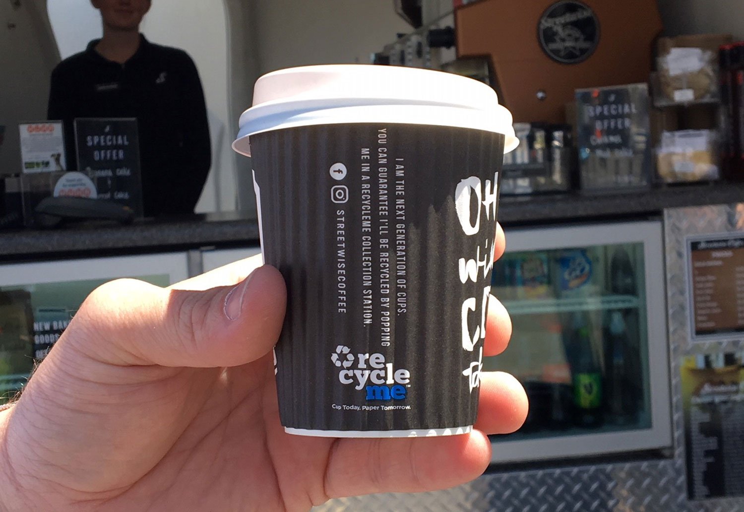 Image of Streetwise Coffee Cup held in front of a Streetwise Coffee Cart