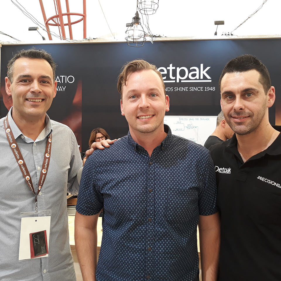 Image of Precision Series winner, Glenn Bailey standing next to Adam Genovese from Genovese coffee and Clint Hendry from Detpak at the Detpak stand at MICE 