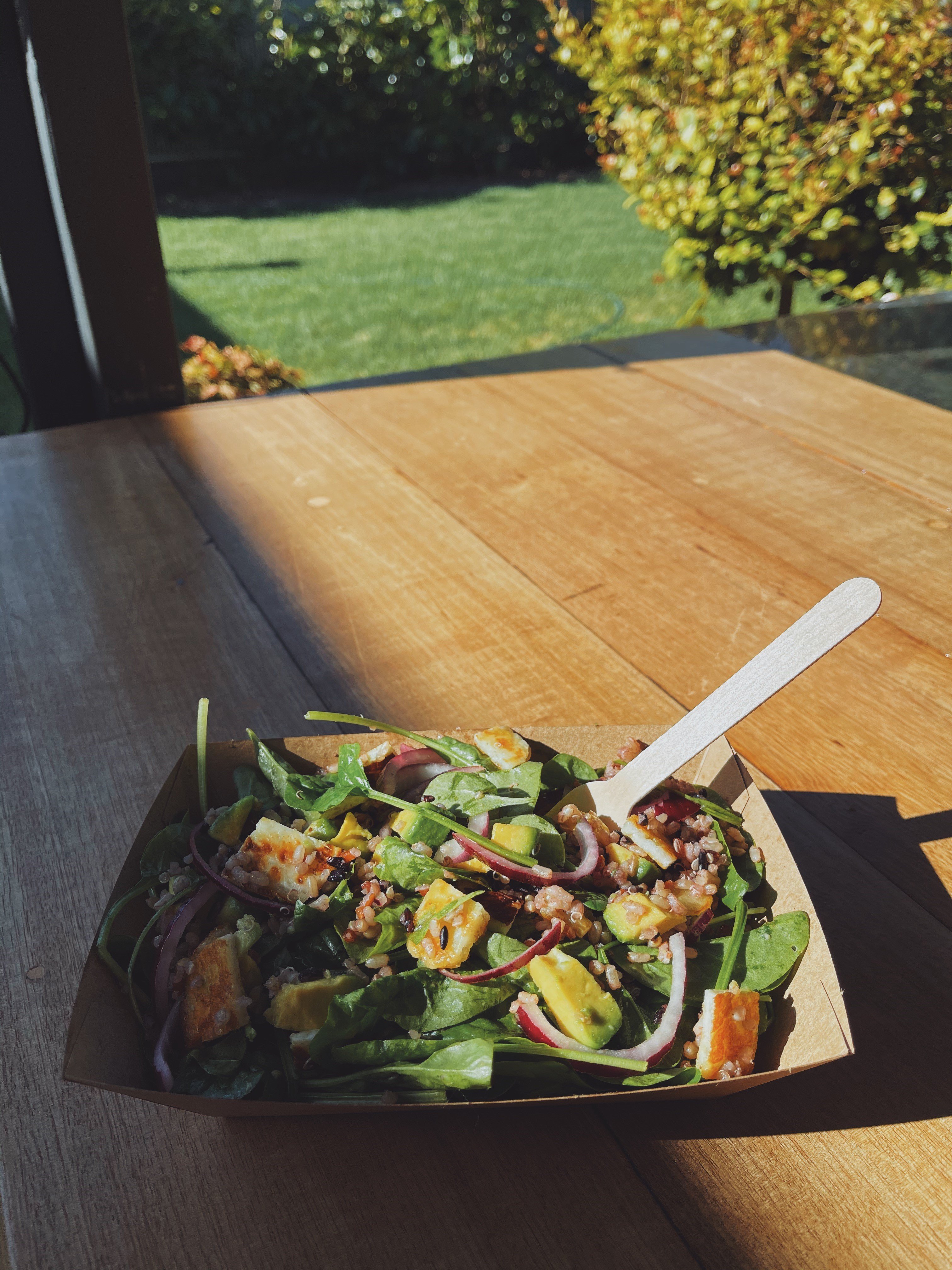 Endura tray filled with salad pictured on the beach with a wooden fork. 