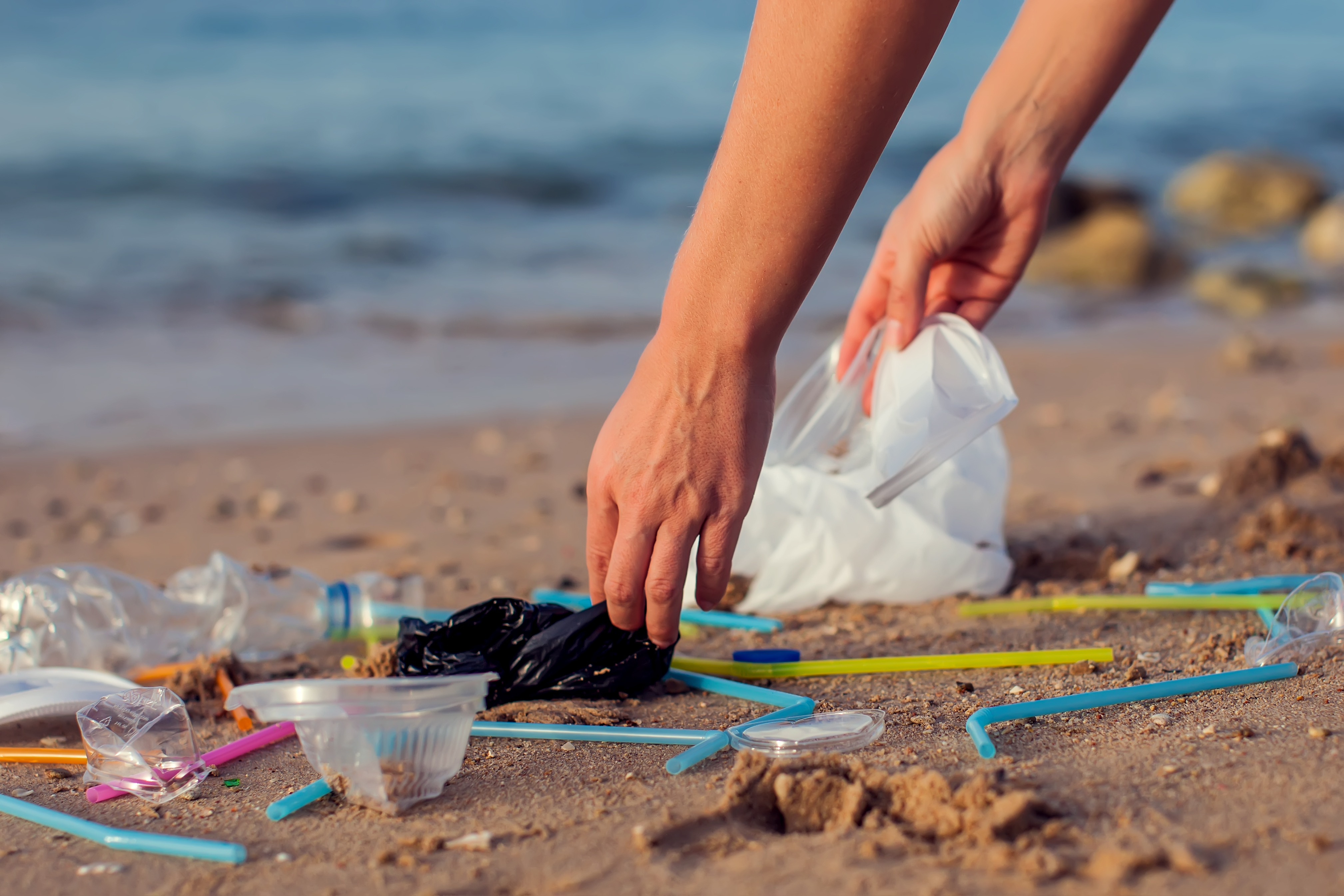 Person picking up plastic waste on the beach. 