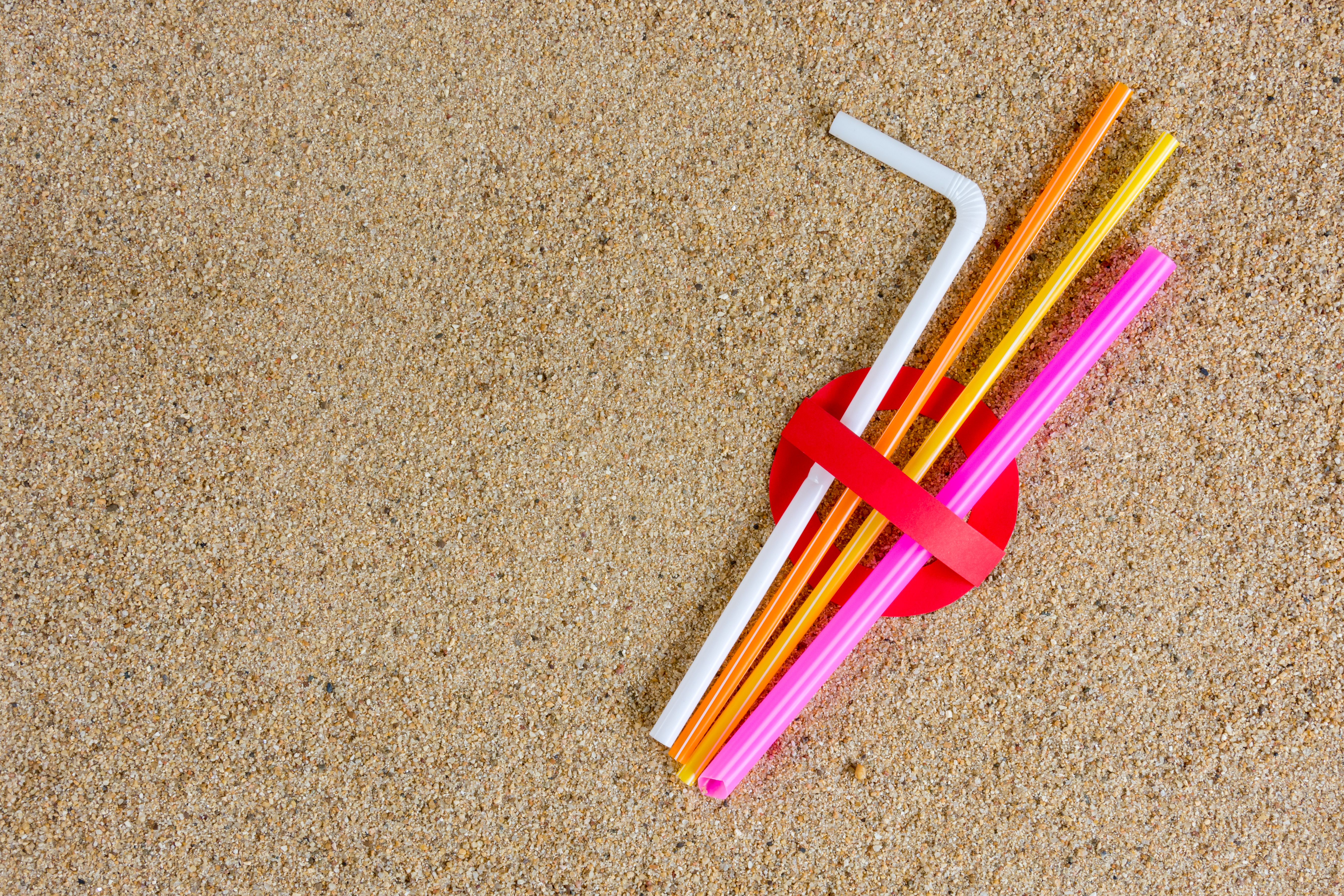 Plastic straws in banned symbol on beach sand.